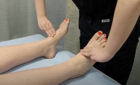 A clinician palpating dorsalis pedis pulses on the tops of both feet.